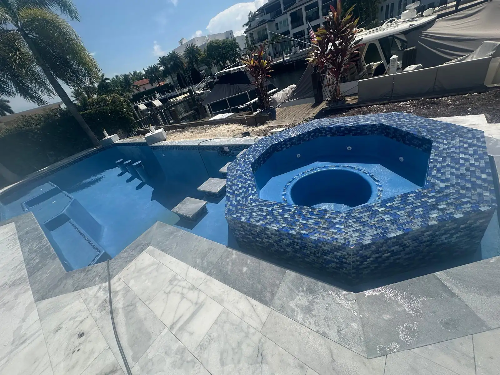 Raised spa with blue glass tile next to a waterfront pool