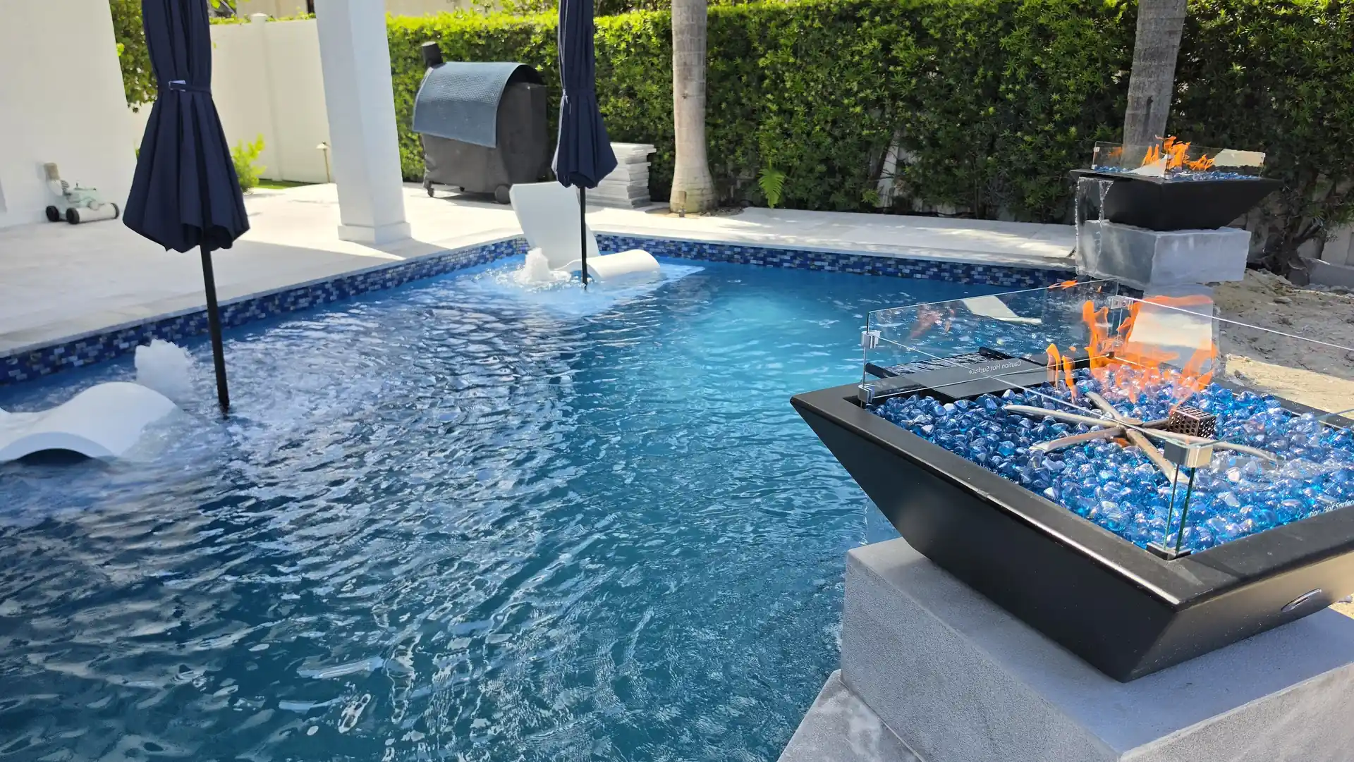Glass fire bowl beside a blue pool with in-water loungers